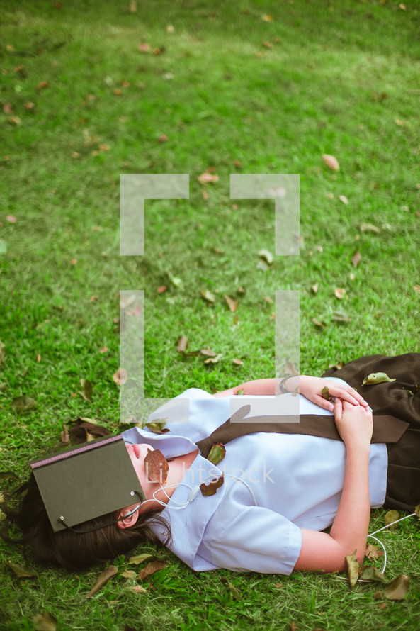 a girl sleeping in the grass with a book covering her face 