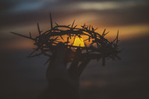 silhouette of a man holding up a crown of thorns at sunset 