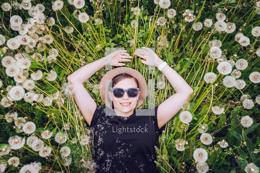Young beautiful girl in sunglasses lies in dandelion field and looks to the sky. Top view