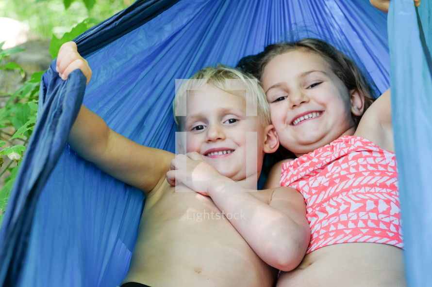 Smiling boy and girl in a blue hammock.