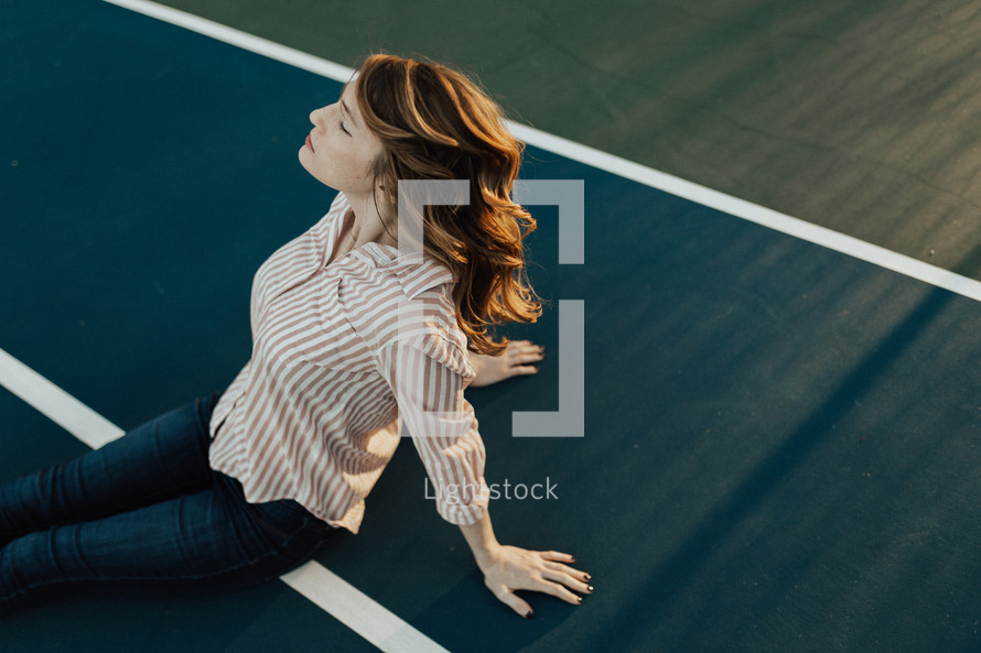 portrait of a woman sitting on a  tennis court feeling the sunlight on her face 