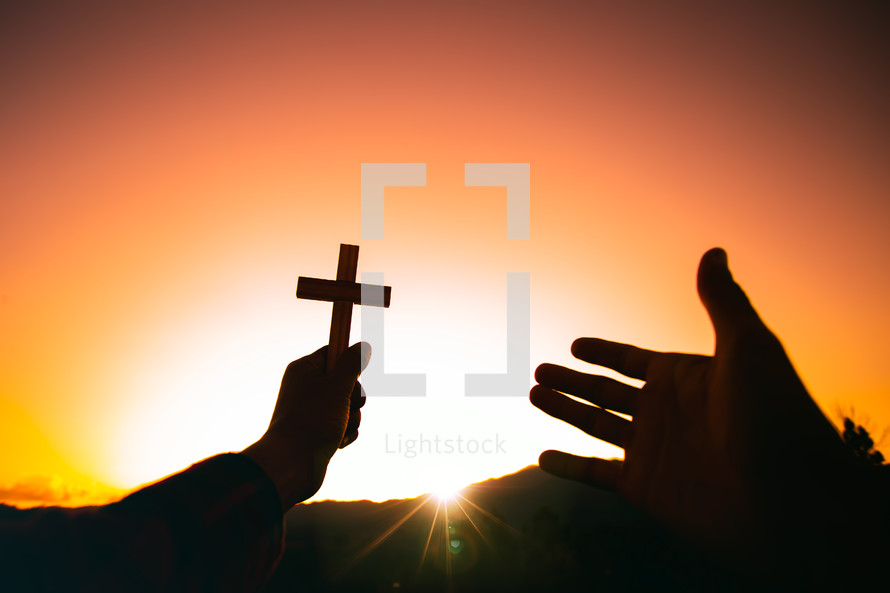arms holding up a cross against an orange sky 