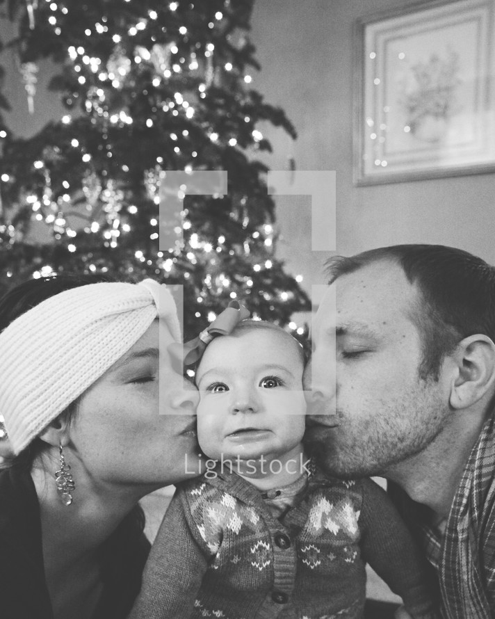 mother and father kissing their infant daughter at Christmas 