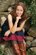 portrait of a brunette woman in tall boots and a dress sitting outdoors 