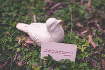 A card with a scripture and a ceramic bird among vegetation.