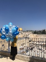 a woman holding balloons looking out a the wailing wall in Jerusalem 