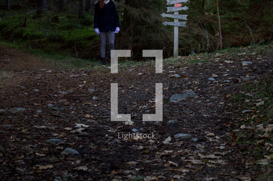 a woman standing by a sign in a forest determining direction to take 