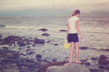 girl with a sand bucket walking on a rocky beach 