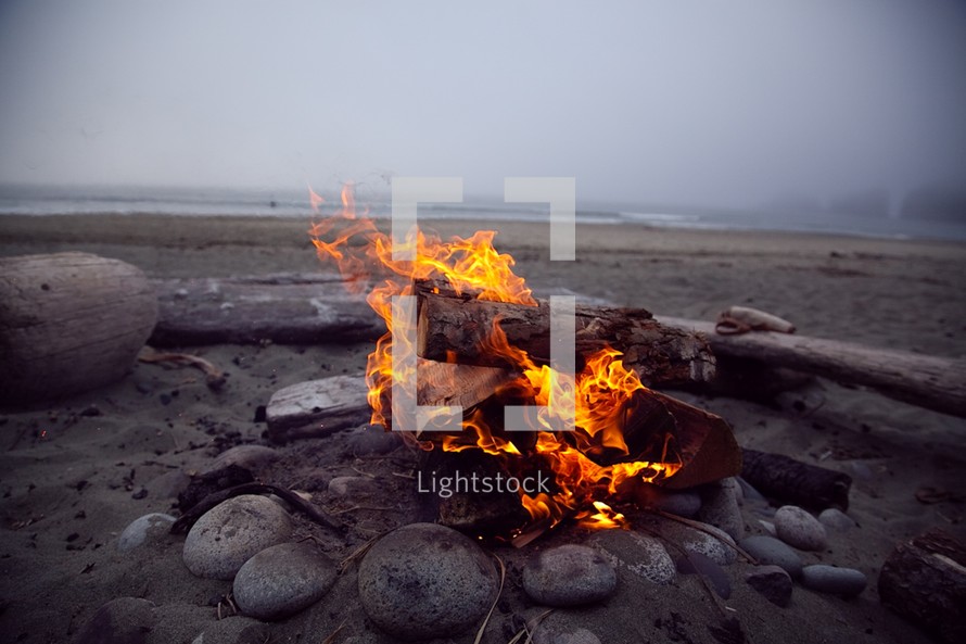 A fire in a fire pit on the beach.