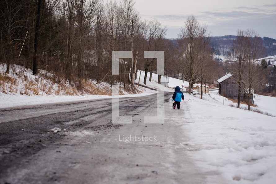 a child walking in snow along a rural road 
