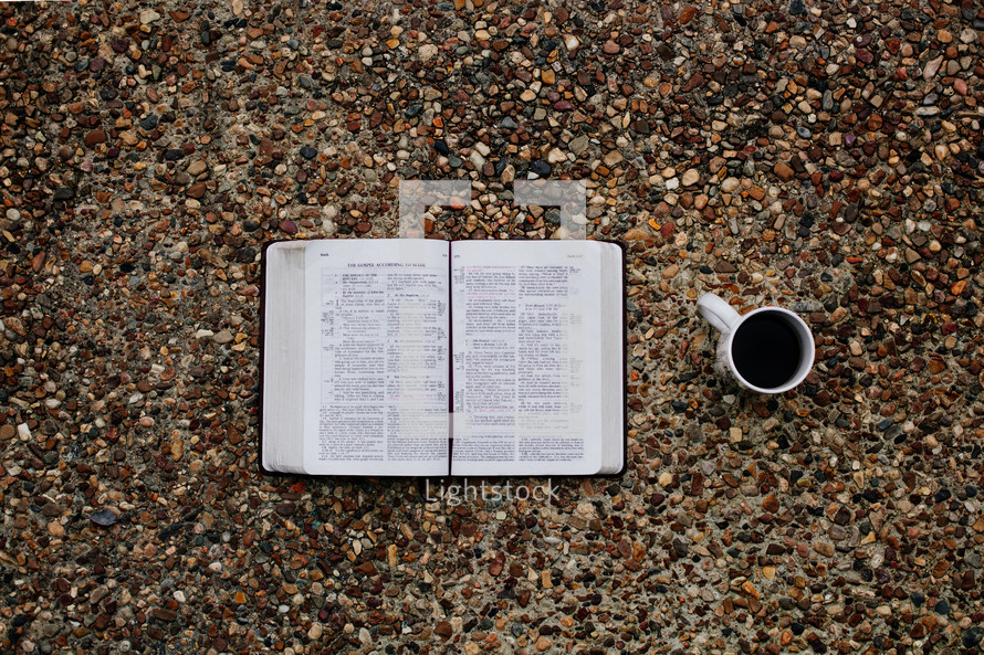 open Bible and coffee mug on gravel