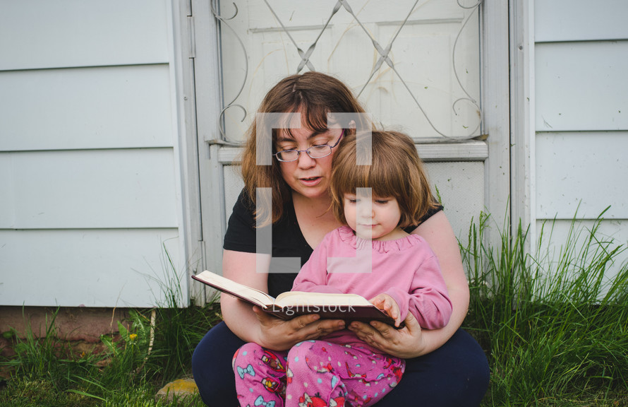 mother and daughter reading a Bible together outdoors