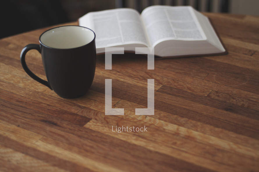open Bible on a wood table and coffee mug 