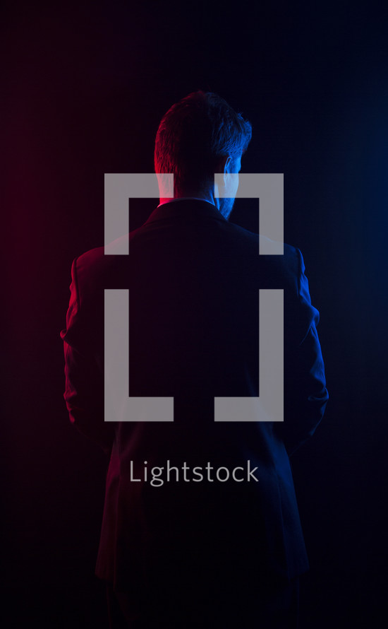 Red and blue light shining on the back of a man in a suit.
