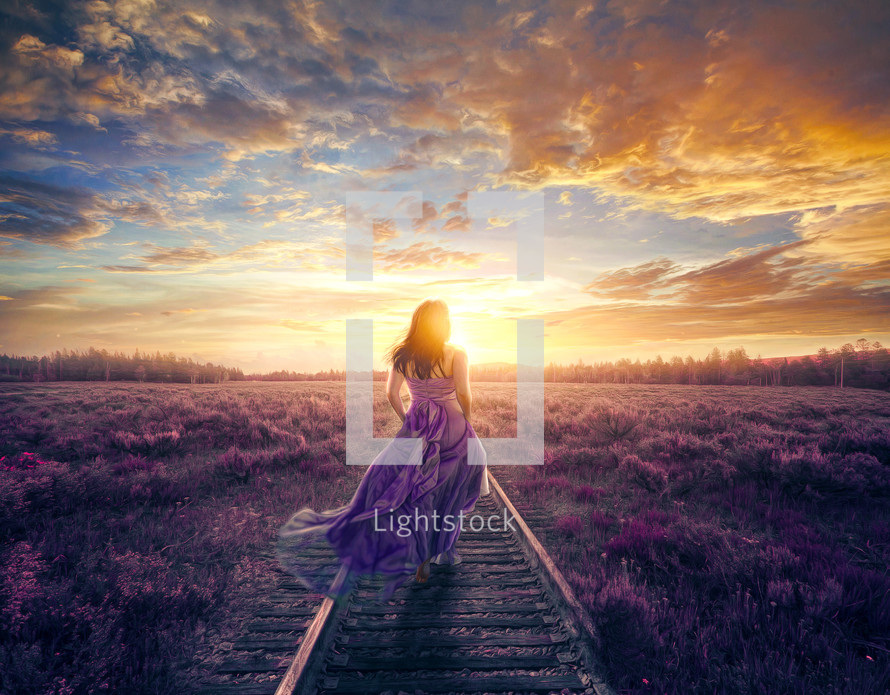 A woman in a colorful purple dress walks to a beautiful sunset.