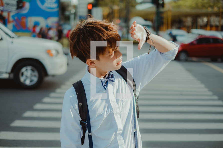teen boy crossing a city street and shading sunlight from his eyes 