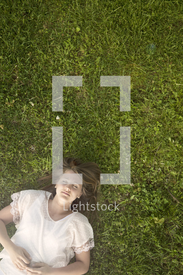 Teen girl with eyes closed laying a field of green grass.