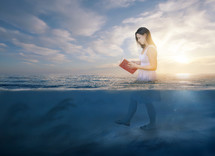 a woman walking in ocean water reading 
