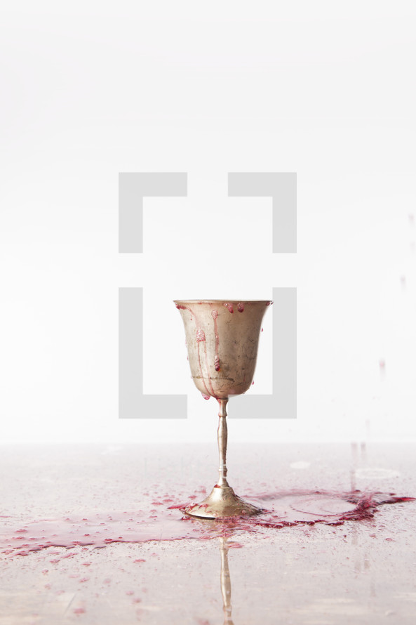 red wine spilling over a chalice onto a table 