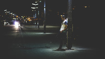 A man leaning against a light pole at night.