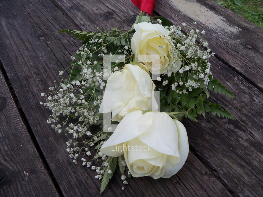A bouquet of white roses surrounded by babies breathe draped over an old wooden bench for a special wedding day, valentines day or any celebration of love between  a man and a woman. 