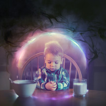 A small boy prays at the kitchen table with darkness trying to get close to him