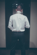 A man standing in front of a mirror putting on a tie.