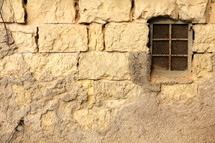 Barred window in weathered stone wall 