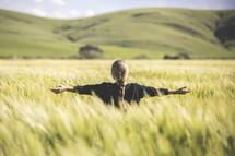 a woman standing in a field of wheat with outstretched arms 