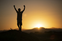 teen boy standing in warm sunlight with arms raised 