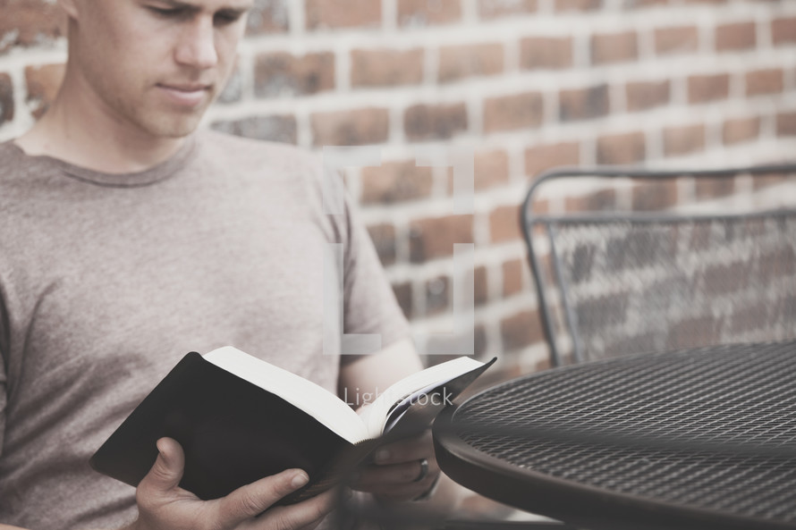 man reading a Bible outdoors sitting at a table 
