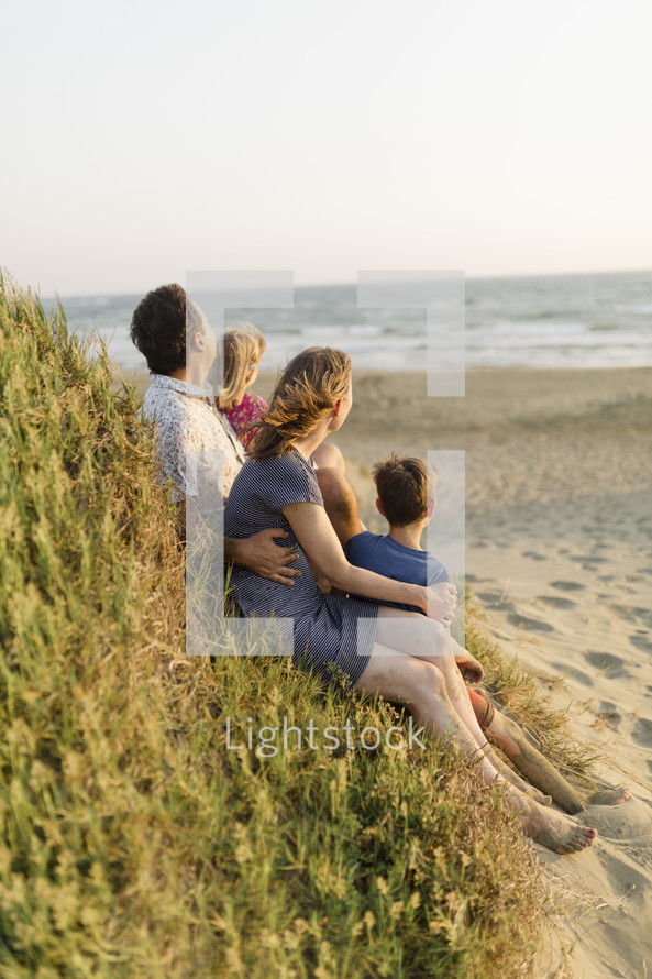 Family of four sitting on the beach at sunset.