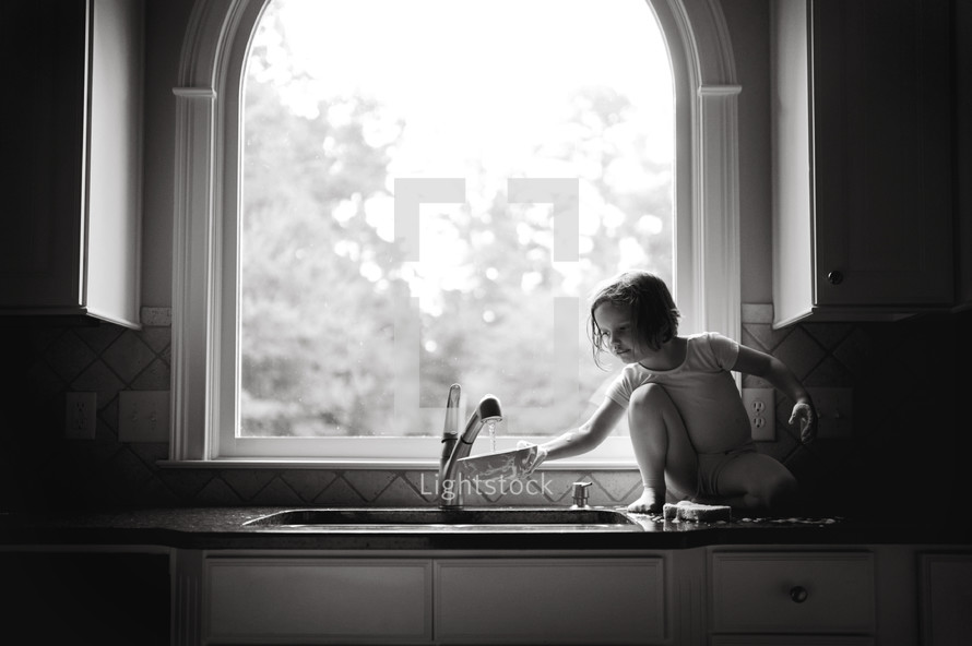 girl child standing on the kitchen counter at the sink 