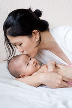 An Asian mother kissing her newborn baby 