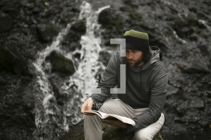 a man sitting on a rock reading a Bible 