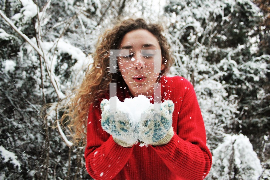 a woman with cupped hands blowing snow