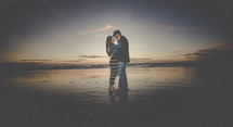 A young couple embrace on the beach in the moonlight.