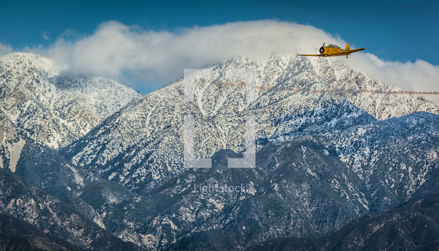 vintage single engine aircraft flying over mountains 