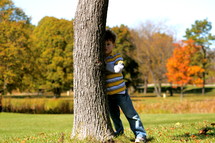 a boy child hiding behind a tree 