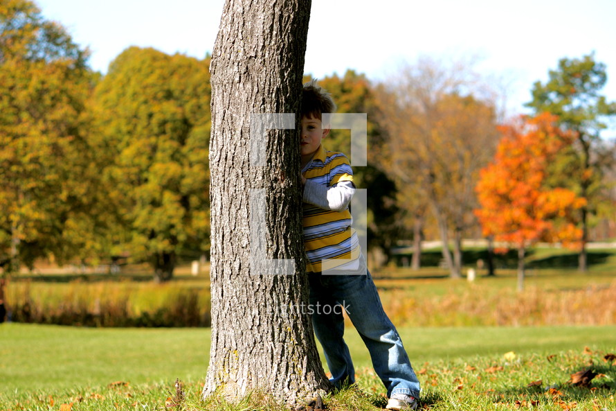 a boy child hiding behind a tree 