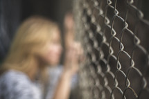 a woman looking through a chain link fence 