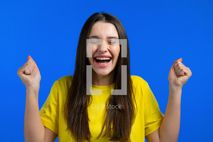 Woman is very glad and happy, she shows yes gesture of victory, she achieved result, goals. Surprised excited happy lady on blue studio background. Jackpot concept. High quality photo