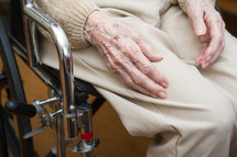 Hands of an elderly person sitting in a wheelchair.