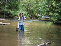 a teen girl with a net walking in a stream 