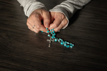 Hands holding a rosary on a dark wood table