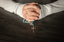 Hands holding a rosary on a dark wood table