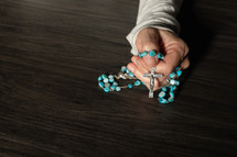 One hand holding rosary on a dark wood table