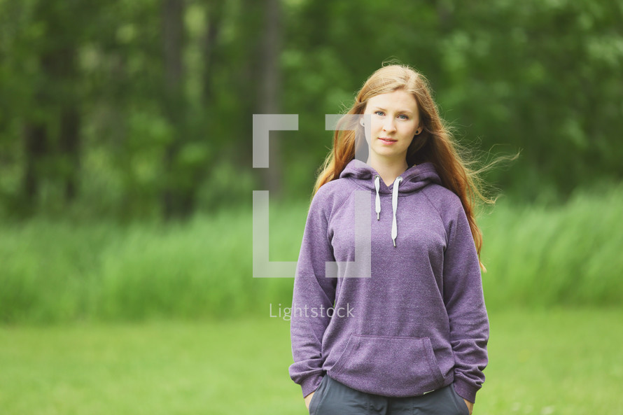 a teen girl in a hoodie standing outdoors 