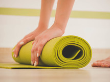 Process of preparing for class. Young woman rolls apart green yoga mat in fitness studio. Freedom, health lifestyle concept. Close up shot