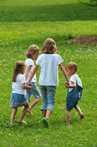 Siblings holding hands and walking through the grass.